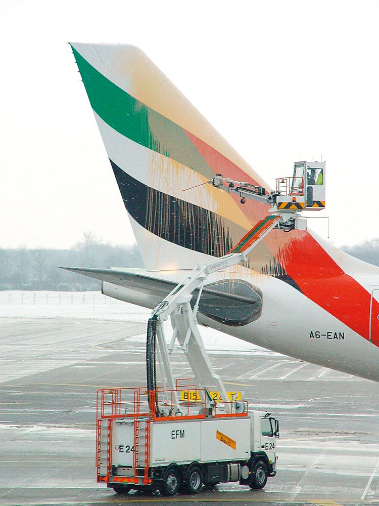 Emirates aircraft tail with green, black, and red stripes; maintenance vehicle with lift servicing the tail section.