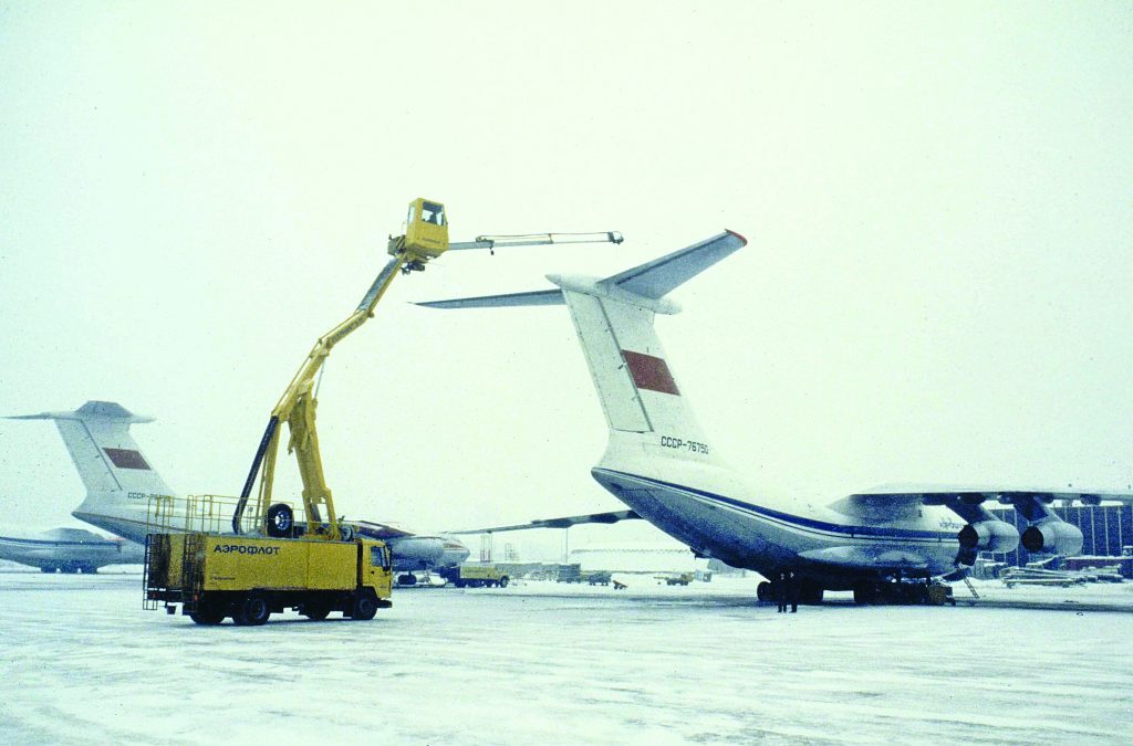 A yellow lift truck servicing the tail of a large aircraft in a snowy airport environment.