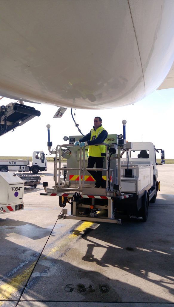 A worker in a safety vest operates equipment to service an aircraft on the tarmac.