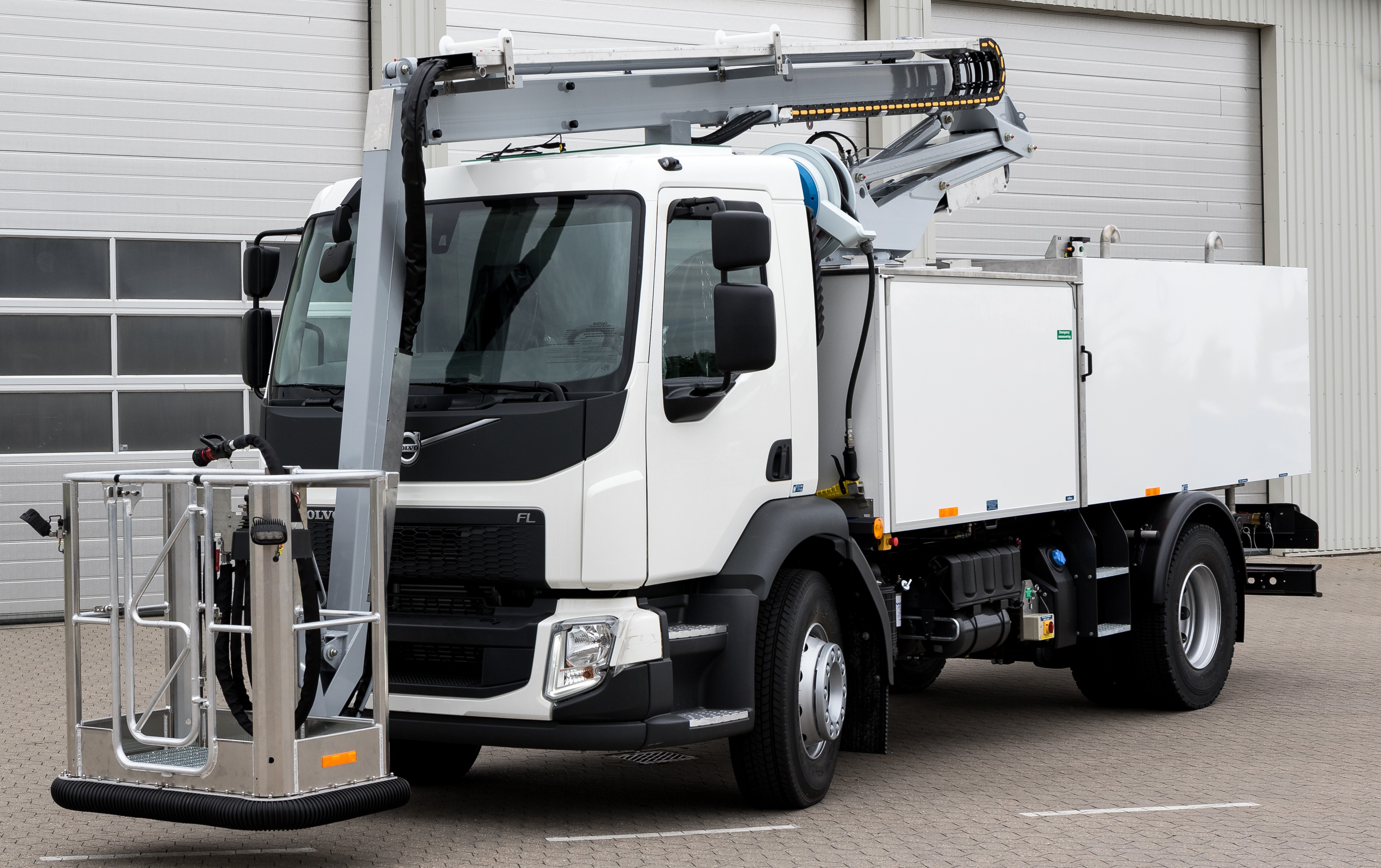 White utility truck with an elevated platform and crane, parked in front of a garage.