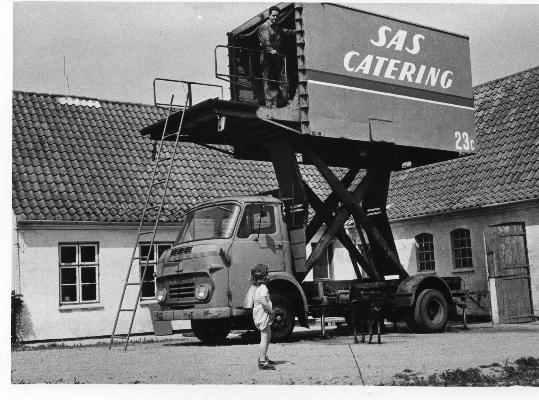 SAS Catering container on a lift truck, with a child standing nearby and a ladder leaning against the truck.