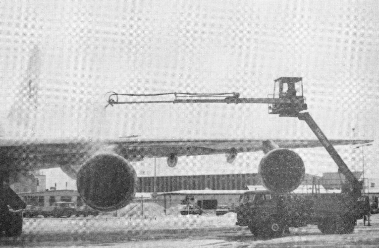 A truck with a lift sprays de-icing fluid on the wing of a large airplane at an airport during winter.