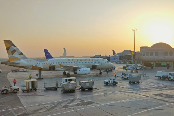 Etihad Airways aircraft parked at sunset, with ground service vehicles and terminal in the background.