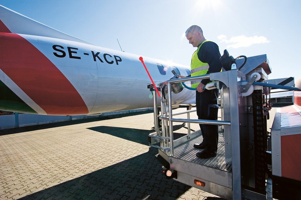 Ground crew member in a safety vest operates equipment next to the aircraft registered SE-KCP on the tarmac.