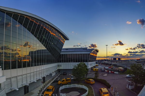 Panoramic view of an airport terminal at sunset, featuring modern architecture and yellow taxis in the foreground.