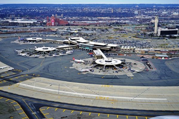 Aerial view of an airport terminal with multiple aircraft, parking areas, and surrounding cityscape.