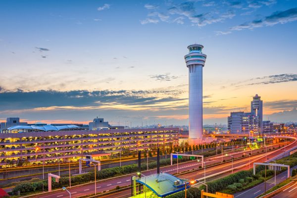 Airport control tower at sunset, with roads and buildings visible in the foreground.