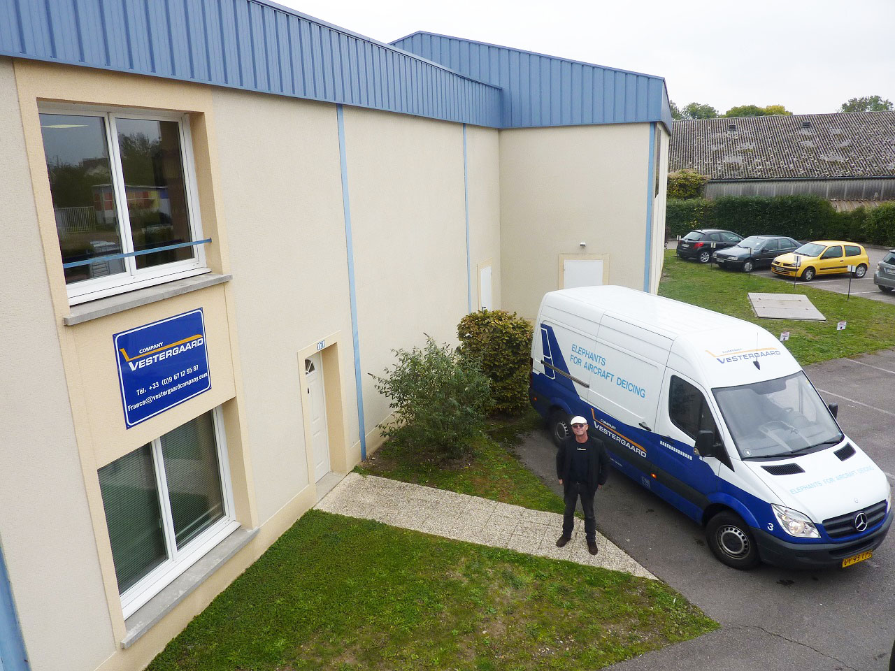 Delivery van parked outside a building with a sign, and a person standing next to it.
