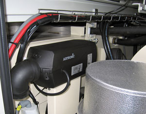 Autronic device with black casing and connected pipes, situated among various machinery components.