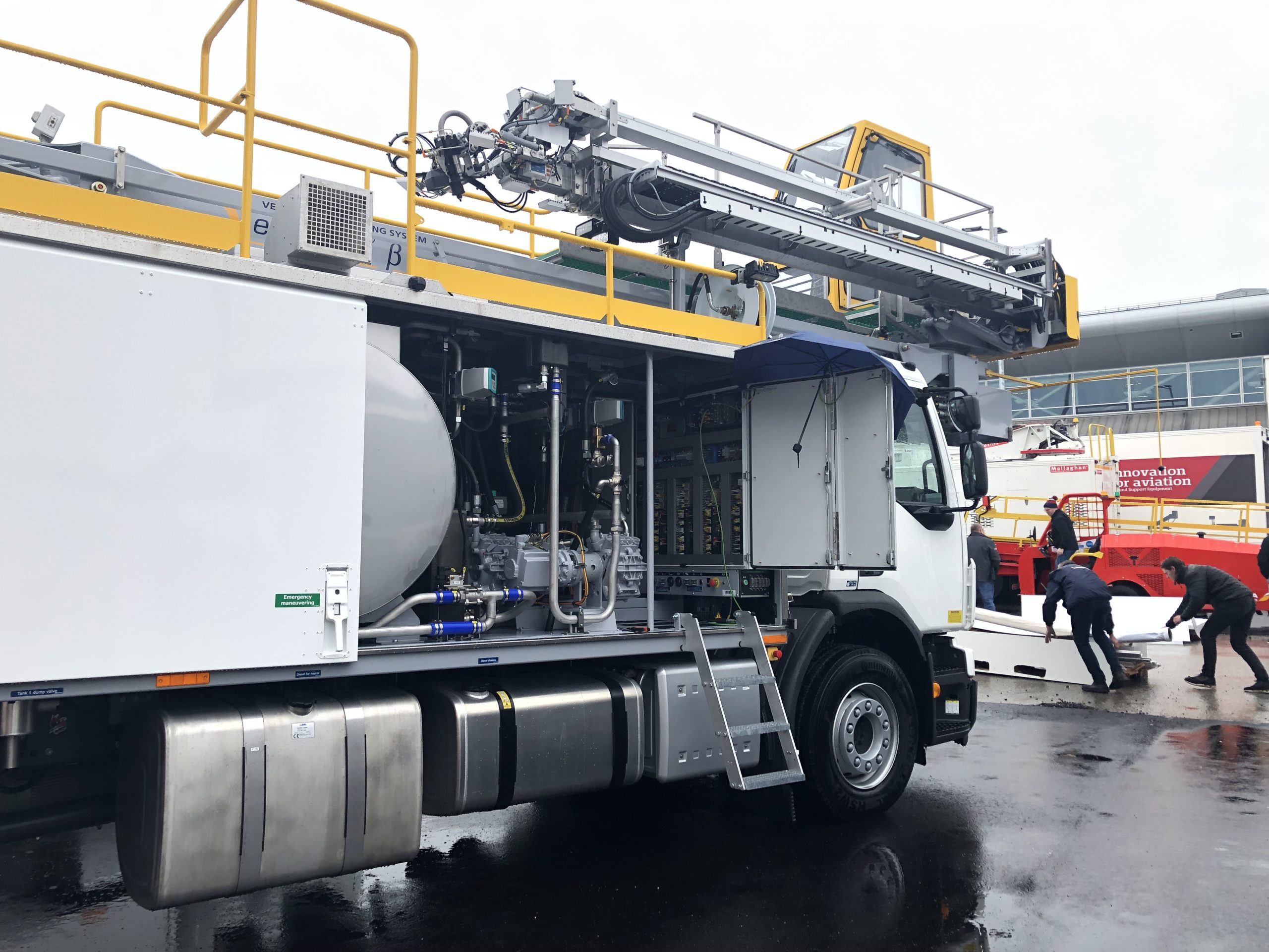 Firefighting truck with a ladder and equipment, parked on a wet surface, with personnel nearby.