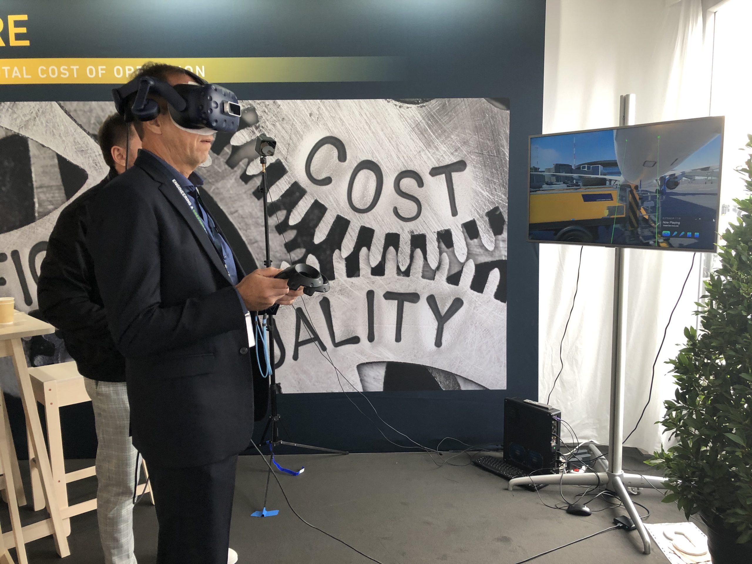 A man in a suit uses a VR headset while interacting with a screen displaying a virtual environment.