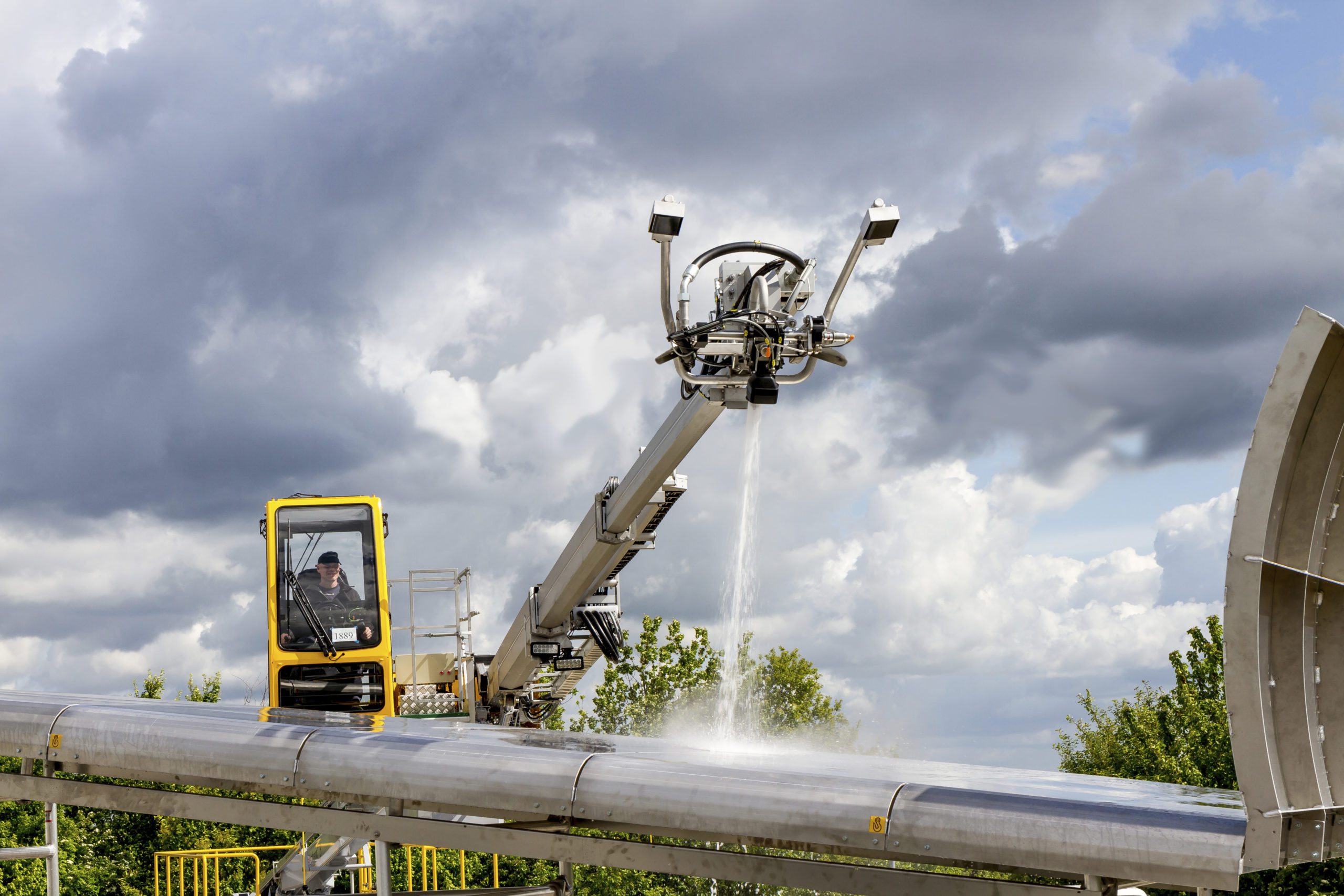 A machine spraying water on a large pipe, with a person operating it from an enclosed cabin.
