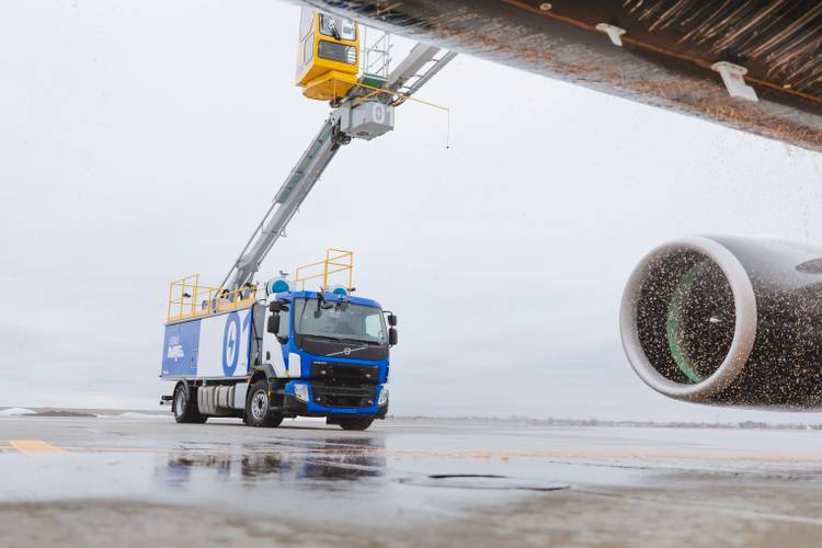 A blue and white aircraft maintenance truck with a raised platform working near a jet engine on a rainy day.