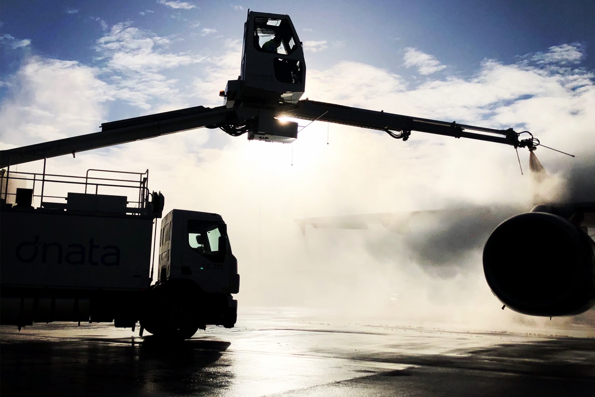 Dnata ground handling equipment servicing an aircraft with a large circular engine, silhouetted against a cloudy sky.